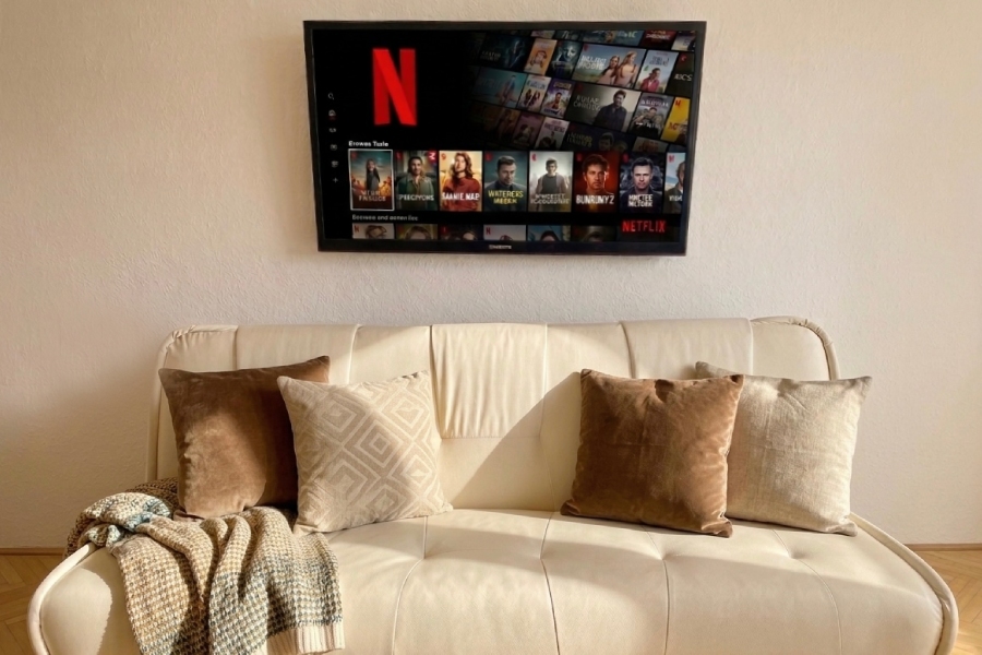 Biela pohovka s vankúšmi a prikrývkou, nad ňou televízor s logom Netflix a ponukou seriálov.